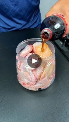 a person pouring sauce into a container filled with meat on top of a black table