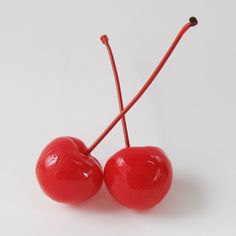 two red cherries sitting side by side on a white surface, with one cherry still attached to the other