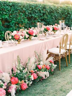 a long table with pink and white flowers on it is set up for an outdoor dinner