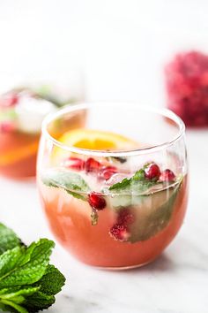 two glasses filled with drinks and garnished with mint, lemon, and pomegranate