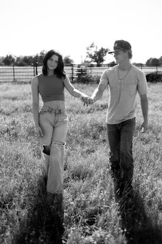 a man and woman holding hands while walking through the grass in a fenced field