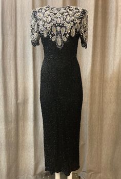 This is amazing full length dress was designed by Laurence Kazar in the 1980s. It is made of silk covered in black glass beads with silver and white sequins and beads in a paisley style pattern, covering the upper torso. It also comes fully lined. Details include beaded hemline and edges, large key hole at back with zip at the back, long split at the back of dress and scalloped edges to arm sleeves. There are some beads missing here and there but this is barely noticeable when worn. A sticky label was left on the inside edge of the back opening and this has left a bit of residue. Please ask for further photos if required. Vintage Black Fitted Sequin Dress, Black Fitted Vintage Sequin Dress, Vintage Fitted Black Sequin Dress, Vintage Black Sequin Evening Dress, Vintage Black Sequin Dress For Evening, Elegant Beaded Sequin Evening Dress, Black Vintage Evening Dress With Sequins, Elegant Beaded Sequin Dress For Gala, Vintage Black Embellished Evening Dress