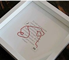 a white frame with a red string in it on top of a wooden table next to a piece of paper