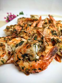 a white plate topped with shrimp and broccoli covered in seasoning next to a purple flower