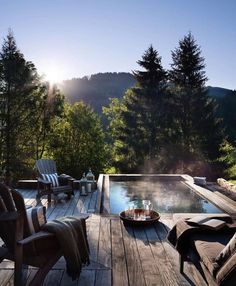 a wooden deck with two chairs and a tray of food on it, overlooking a pool