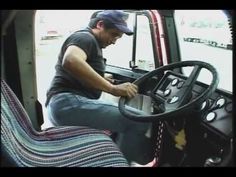 a man sitting in the driver's seat of a truck with his hand on the steering wheel