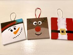 three small bags decorated like santa claus, snowman and elf faces on white surface