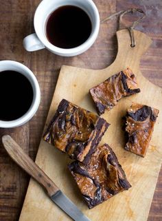 some brownies on a cutting board next to two cups of coffee