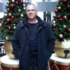 a man standing in front of two large christmas trees with gold and red ornaments on them