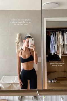 a woman taking a selfie in front of a mirror with clothes hanging on the wall