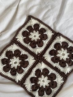 a crocheted square on a bed with white sheets and brown squares in the middle