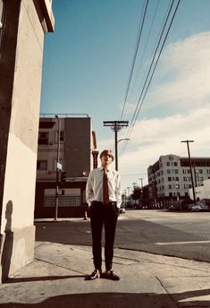 a man standing on the side of a road wearing a shirt and tie with his hands in his pockets