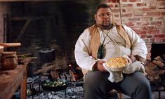 a man sitting in front of a fire holding a plate of food