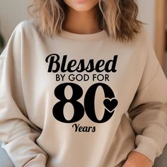 a woman wearing a sweatshirt that says, blessed by god for 80 years