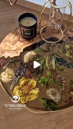 a candle is sitting on top of a glass table with flowers and leaves around it