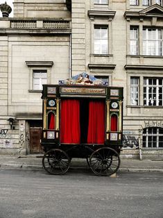 a horse drawn carriage with red curtains in front of an old building on the street