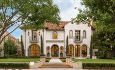 a large white house with lots of windows and trees in the front yard, surrounded by greenery