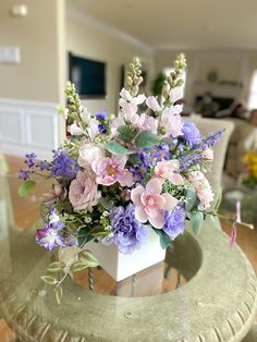 a vase filled with purple and white flowers on top of a glass table in a living room