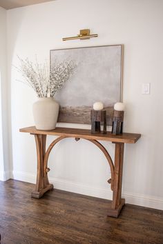 a wooden table with vases and candles on it in front of a white wall