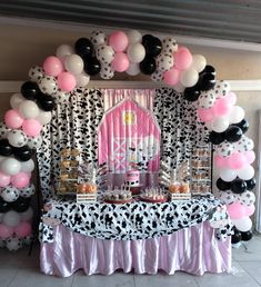 a table topped with lots of balloons and desserts next to a wall covered in cow print