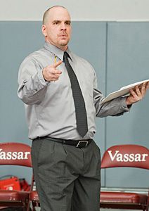 a man standing in front of red chairs holding a clipboard and pointing at something