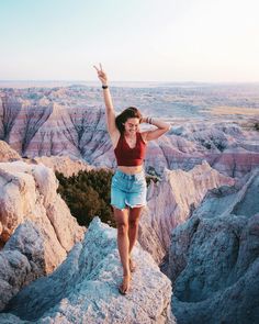 a woman standing on top of a rock with her arms in the air and one hand up