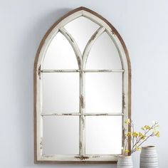 a white vase with yellow flowers sitting next to an arched window mirror on a wall