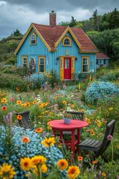 a blue house surrounded by colorful flowers and plants with a red table in the foreground