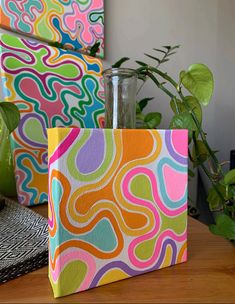 two vases sitting on top of a wooden table next to plants and boxes with designs painted on them