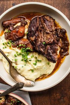 a white bowl filled with meat and mashed potatoes on top of a wooden table