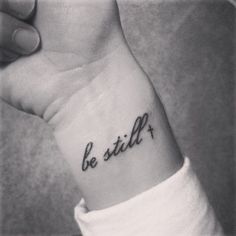 a woman's wrist tattoo with the word be still on it, in cursive font