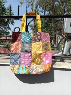 a multicolored patchwork bag hanging from a metal rail with trees in the background