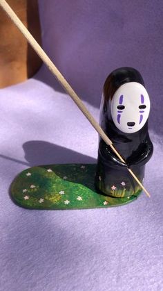 a black and white doll holding a stick on top of a green object with flowers