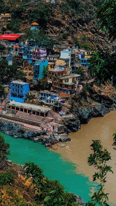 an aerial view of a village on the edge of a cliff with blue water in front of it