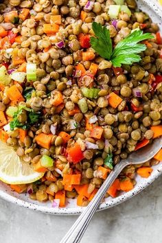 a white bowl filled with lentils, carrots and celery next to a lemon wedge