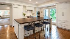 a kitchen with an island and bar stools in the middle of it, surrounded by white cabinets