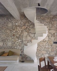 a living room with stone walls and a spiral staircase leading up to the second floor