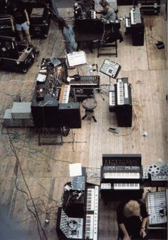 an overhead view of musical instruments and keyboards on a wooden floor with people in the background