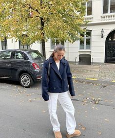 a woman in white pants and a blue jacket is walking down the street with her hand on her hip