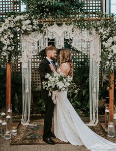 a bride and groom standing in front of an outdoor wedding ceremony arch with greenery