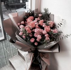 a bouquet of pink roses is tied to the side of a building with a ribbon