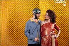 a man and woman standing next to each other in front of a yellow wall with dots