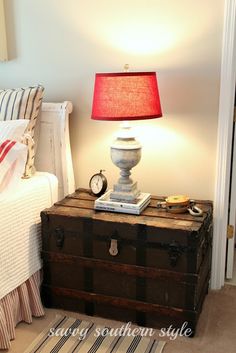 an old trunk with a lamp on top of it in the corner of a bedroom