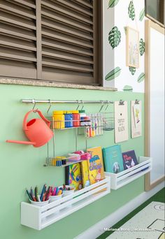 a shelf with books, pencils, and watering can on it next to a window