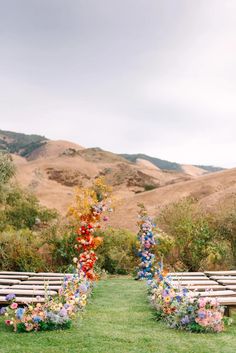 an outdoor ceremony set up with wooden benches and flowers on the back row, in front of mountains