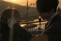 a man and woman standing next to each other in front of a mountain at sunset