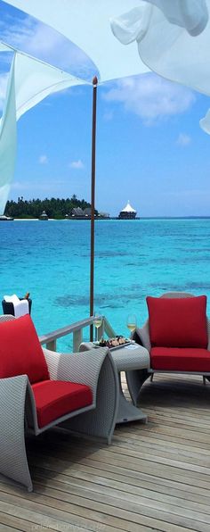 two chairs and an umbrella on a deck near the ocean with blue water in the background