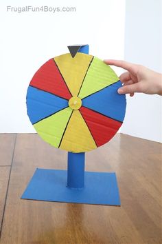 a hand is holding a toy on top of a wooden table with a blue base