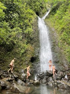 three people jumping off rocks into a waterfall