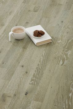 a cup of coffee next to an open book on a wooden floor with a cookie